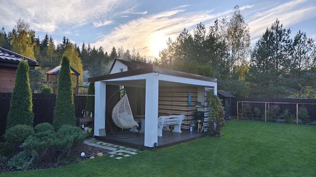 Drewniana altana z ławkami stołowymi i huśtawkami obok koszonego trawnika pod jesienny zachód słońca