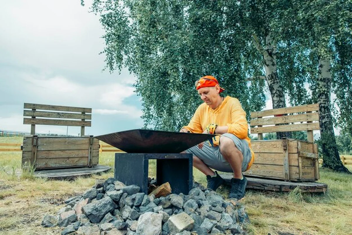 Mężczyzna w żółtej odzieży przy ognisku na zewnątrz z ławeczkami w polu campingowym