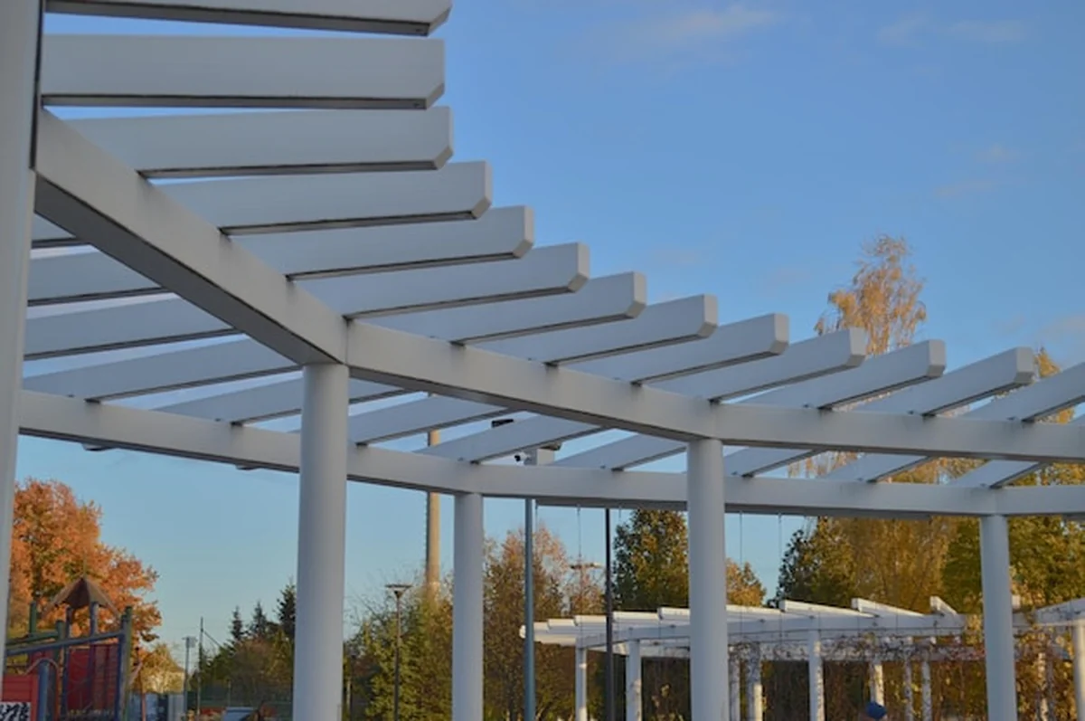 Nowoczesna biała pergola z geometrycznym wzorem belek na tle niebieskiego jesiennego nieba